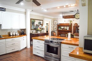 A kitchen with white cabinetry, a stainless steel stove, and a wooden countertop.