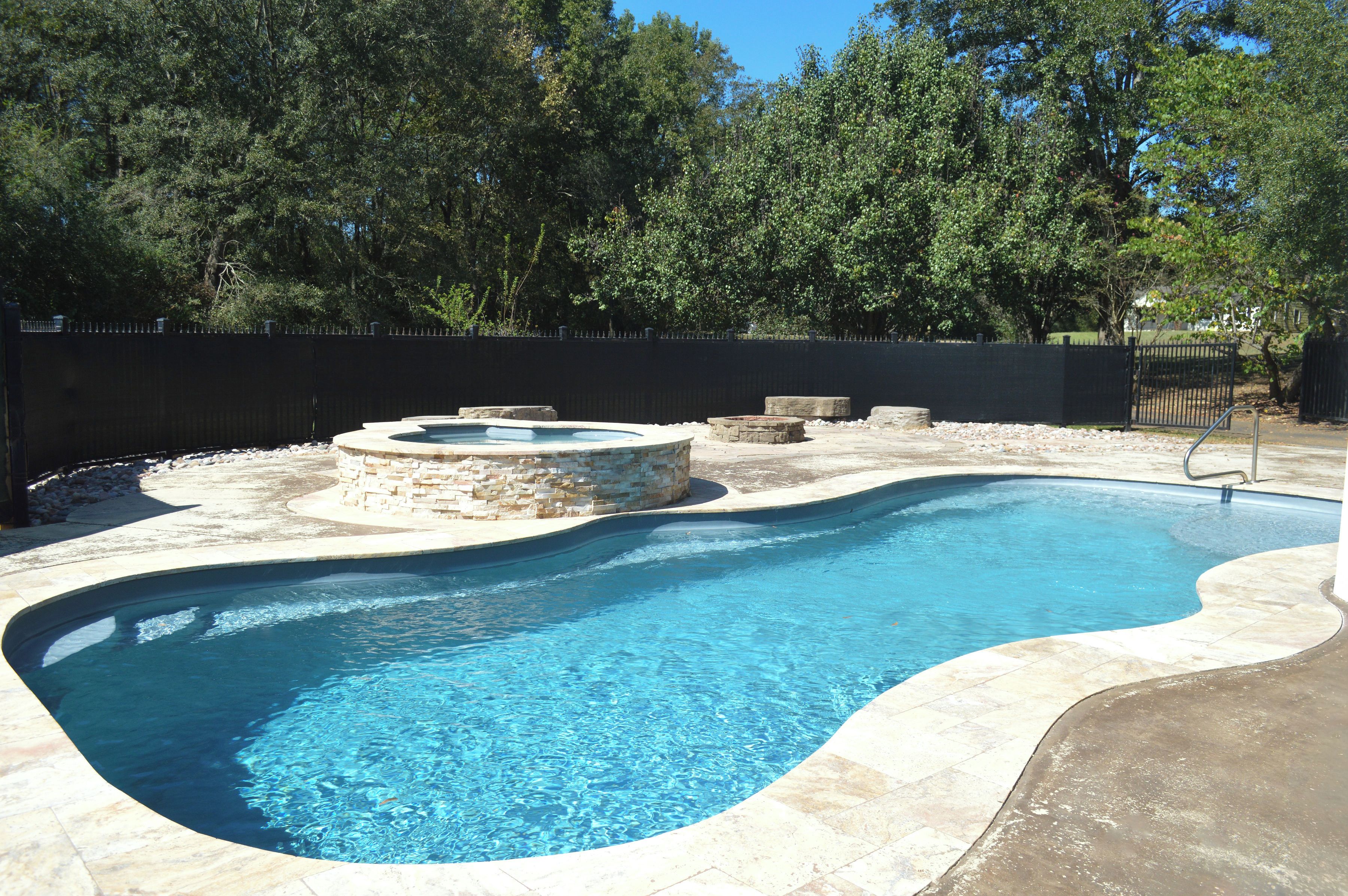 A swimming pool with a stone border and a stone fire pit.