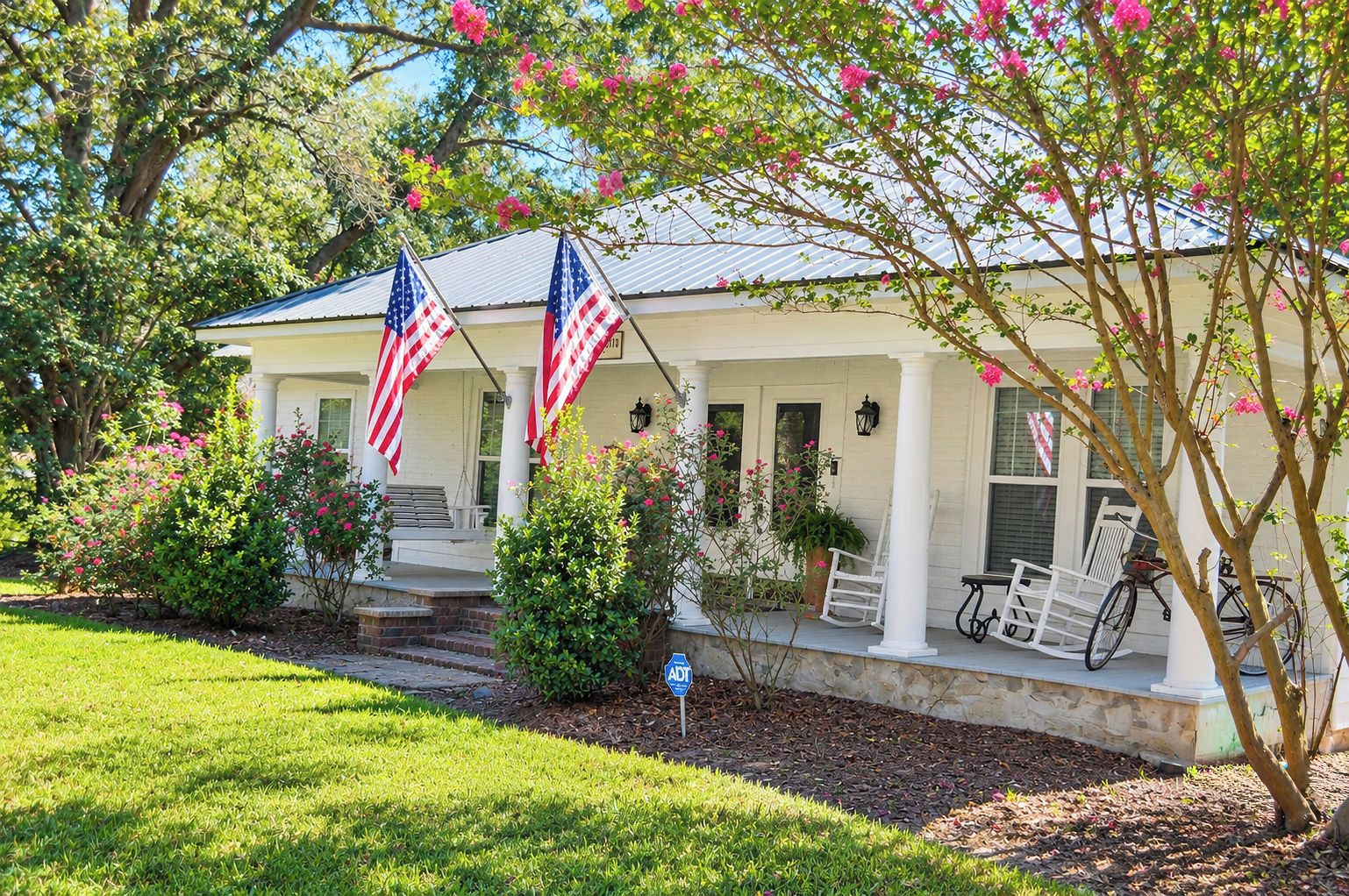 A house with a porch, two American flags, and a bicycle.