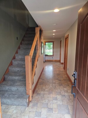 A hallway with a carpeted staircase, a wooden door, and a tiled floor. - House just minutes from the Yellowstone river. (Livingston)