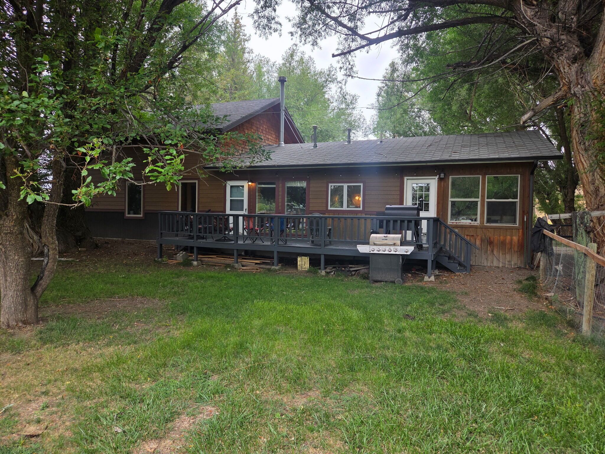 A wooden house with a deck, surrounded by trees.
