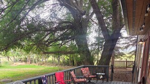 Eine Holzterrasse mit Gartenmöbeln, darunter Stühle und ein Tisch, unter einem großen Baum.