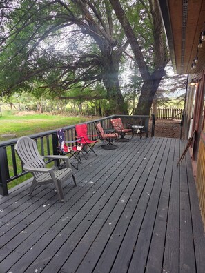 A wooden deck with outdoor furniture, including chairs and a table, under a large tree. - House just minutes from the Yellowstone river. (Livingston)