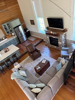 A spacious living room with a stone fireplace, a large sofa, and a kitchen area with modern appliances. - Fabulous 3 bedroom historic 1867 church in charming rural Cedar Falls / Denver. (Cedar Falls)