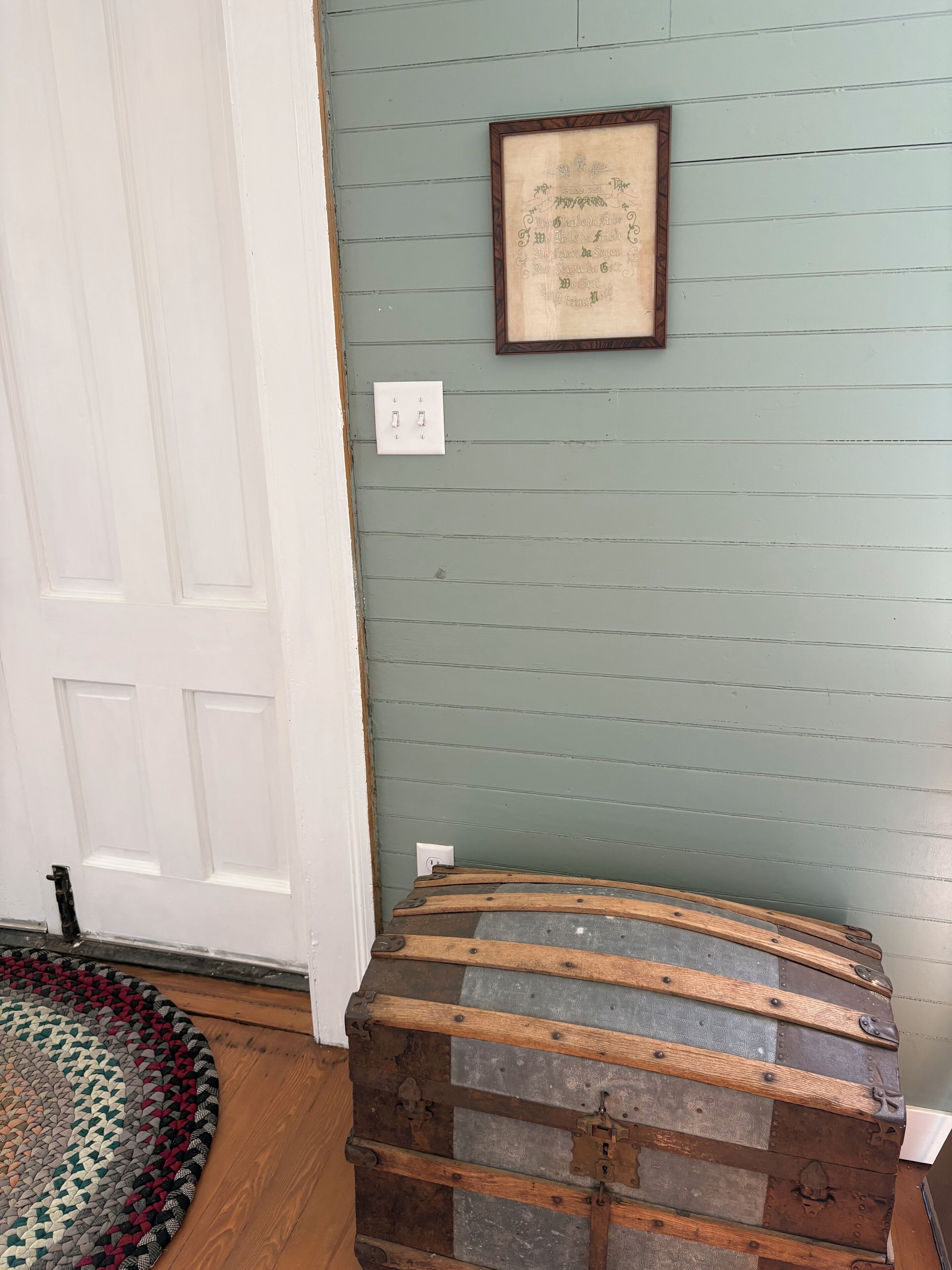 A room with a wooden chest, a framed certificate on the wall, and a door.