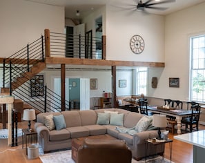 A spacious living area with a high ceiling, a staircase, a dining table, and a cozy seating arrangement.