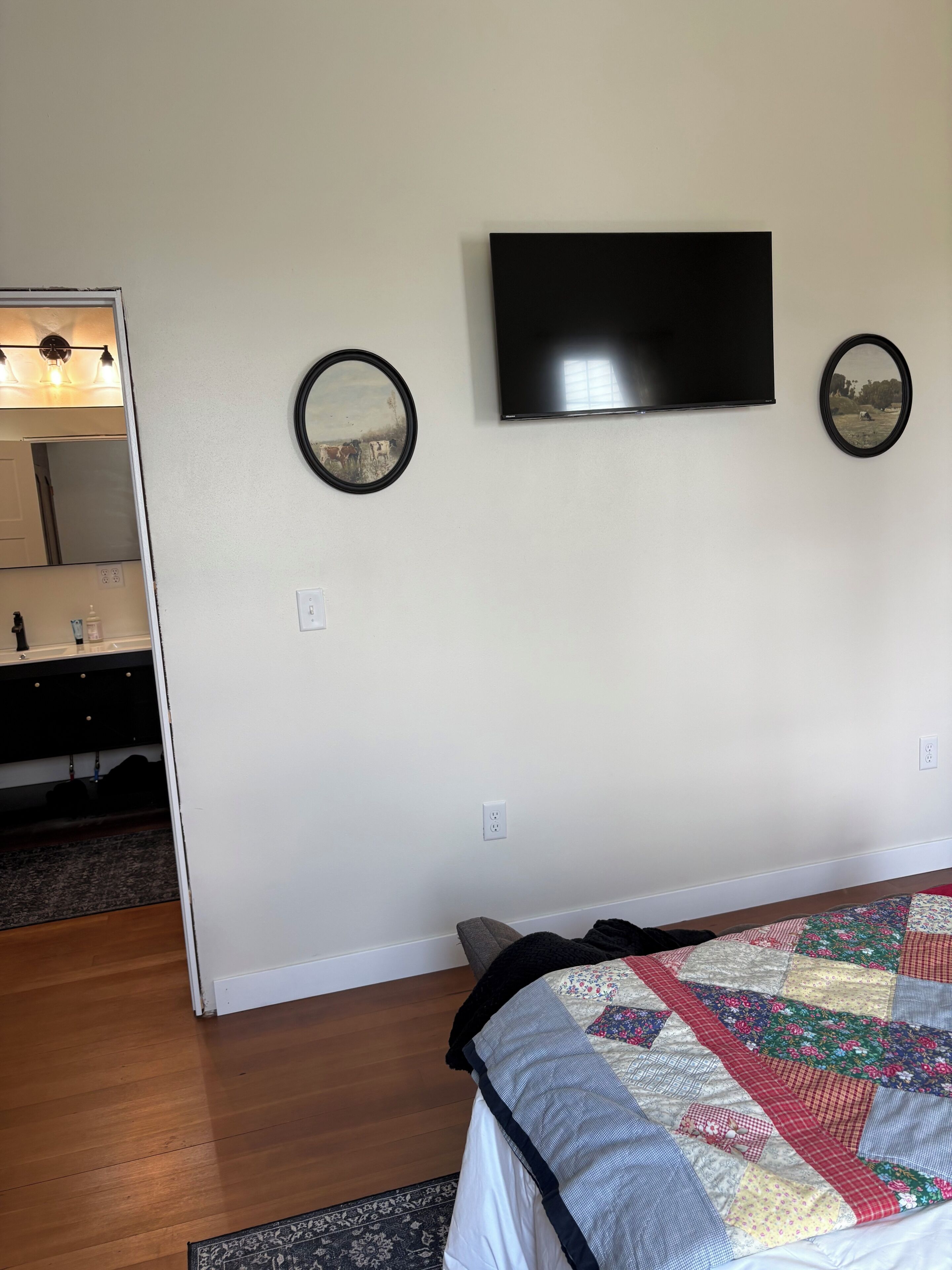 Un dormitorio con cama, televisor, dos espejos en la pared y una puerta que da al baño.