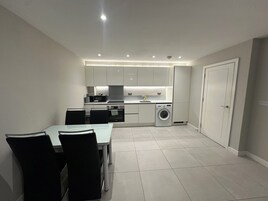 A compact kitchen with modern appliances, a dining area with chairs, and a door.