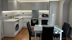 A modern kitchen with built-in appliances, a dining area with a table and chairs, and a washing machine. - High Wycombe Apartments (High Wycombe)