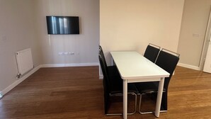 A room with a white table and four black chairs, a flat-screen TV on the wall, and a radiator on the left. - High Wycombe Apartments (High Wycombe)