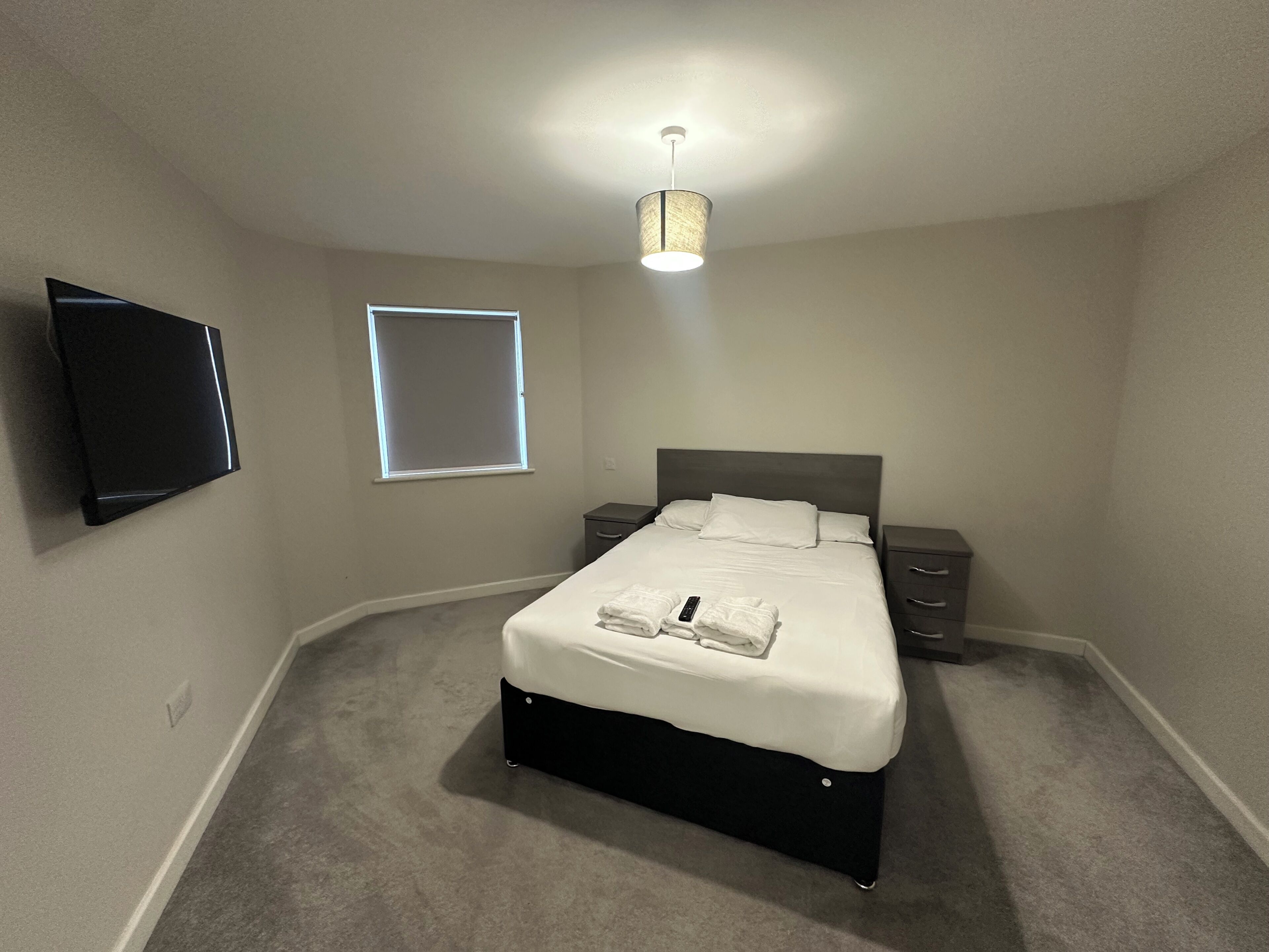 Un dormitorio con cama, mesitas de noche, televisor de pantalla plana y lámpara de techo.