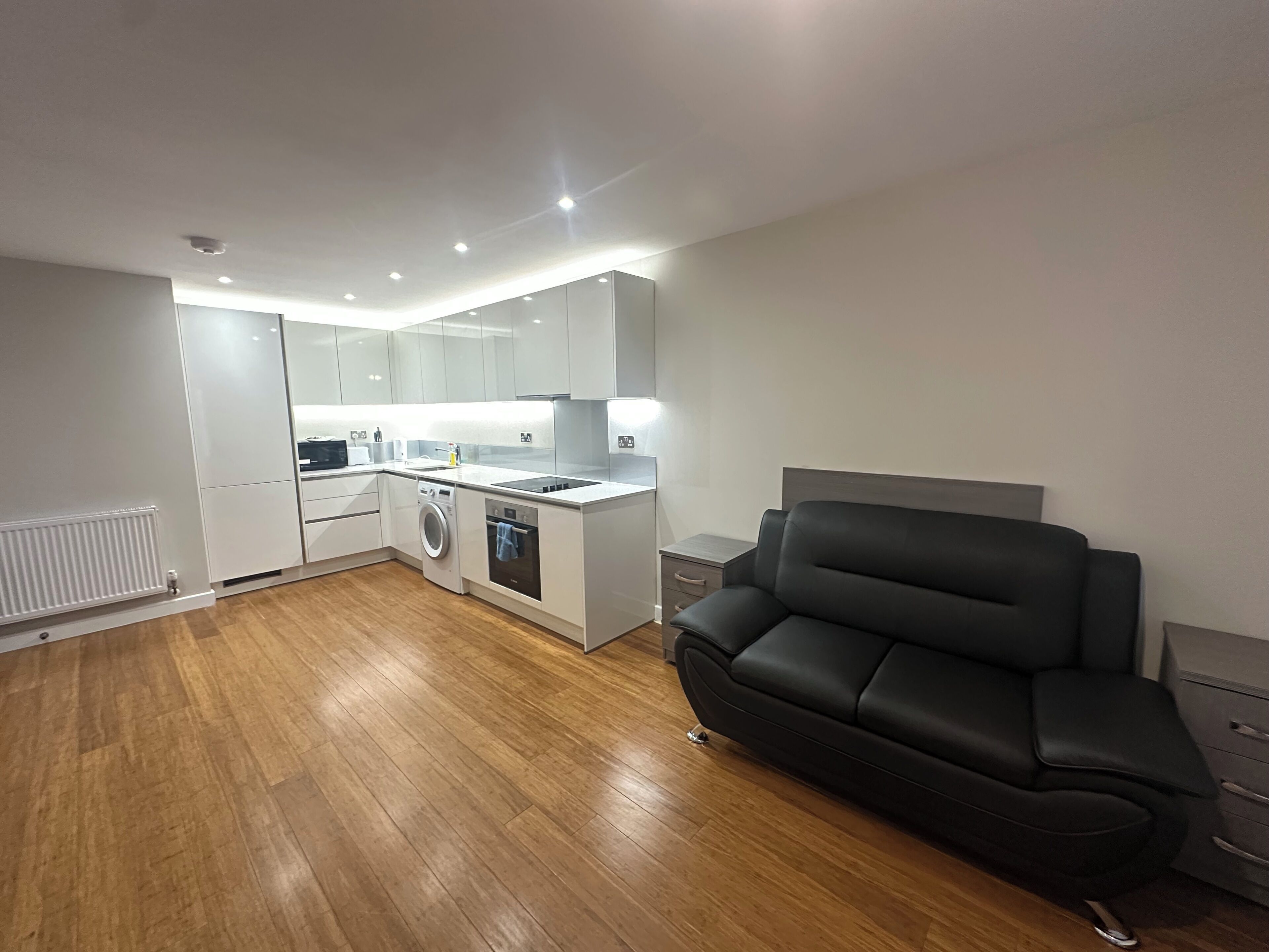 A modern apartment with a kitchenette, a washing machine, a sofa, and a radiator.