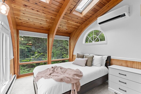 A bedroom with a bed, a bedside table, a window, and a skylight.