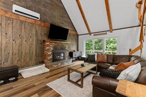 A cozy living room with a brick fireplace, a television mounted on the wall, and a comfortable sofa.