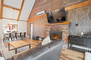 A spacious living area with a fireplace, a television mounted on the wall, and a dining area with chairs and a table.