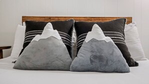 Una cama con cabecera de madera y varios almohadones, incluyendo dos con diseño de montañas.