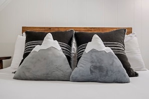 Un lit avec une tête de lit en bois et plusieurs oreillers, dont deux ornés d’un motif de montagne.
