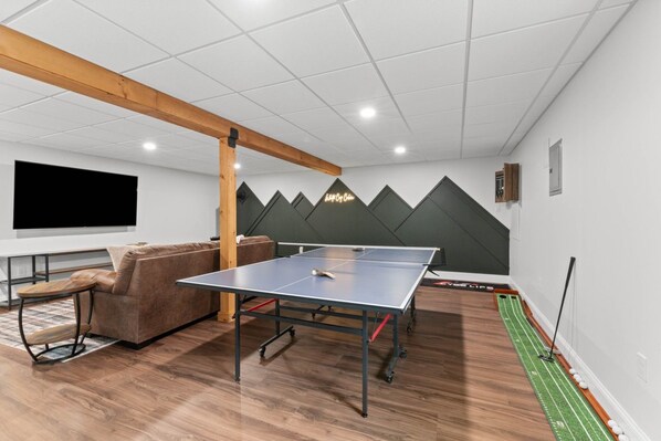 A room with a ping pong table, a sofa, and a television.