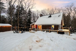 Une cabane dotée d’une terrasse, entourée de neige, et illuminée de guirlandes lumineuses.