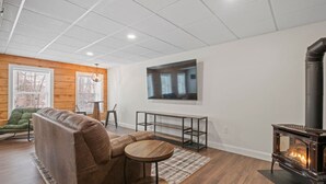 Una sala moderna con un sofá, una mesa redonda de madera, un televisor montado en la pared y una estufa de leña.