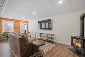 Un salon moderne avec un canapé, une table ronde en bois, un téléviseur fixé au mur et un poêle à bois.
