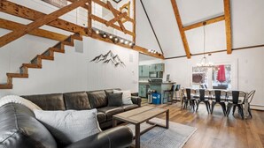 Un amplio salón con sofá de cuero, escalera de madera y zona de comedor con mesa y sillas.