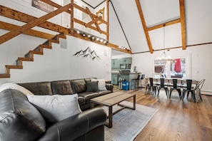 Un vaste espace de vie comprenant un canapé en cuir, un escalier en bois et un coin repas avec une table et des chaises.