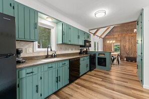 A kitchen with teal cabinets, a wooden ceiling, and a view into a dining area.