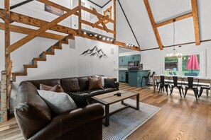 A loft-style living space with a wooden staircase, a sofa, a dining area, and a kitchen.