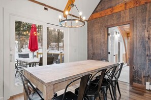 A dining area with a wooden table and chairs, a chandelier, and a view of a snowy outdoor deck.