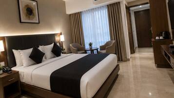 A hotel room with a large bed, bedside tables, a desk, a chair, and a small table with a plant.