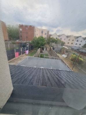 Una azotea con techo metálico, una terraza de madera y vistas a una zona residencial con casas y árboles.