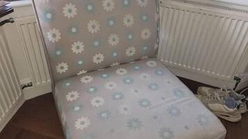 A corner chair with a floral pattern, positioned next to a radiator and a pair of shoes.