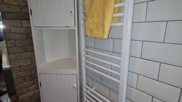 Un baño con pared de azulejos blancos, suelo de madera, un toallero blanco y una toalla amarilla, además de un armario blanco.