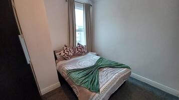 A bedroom with a bed, curtains, a window, and a light fixture.