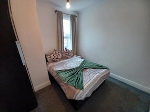 Un dormitorio con cama, cortinas, una ventana y una lámpara.