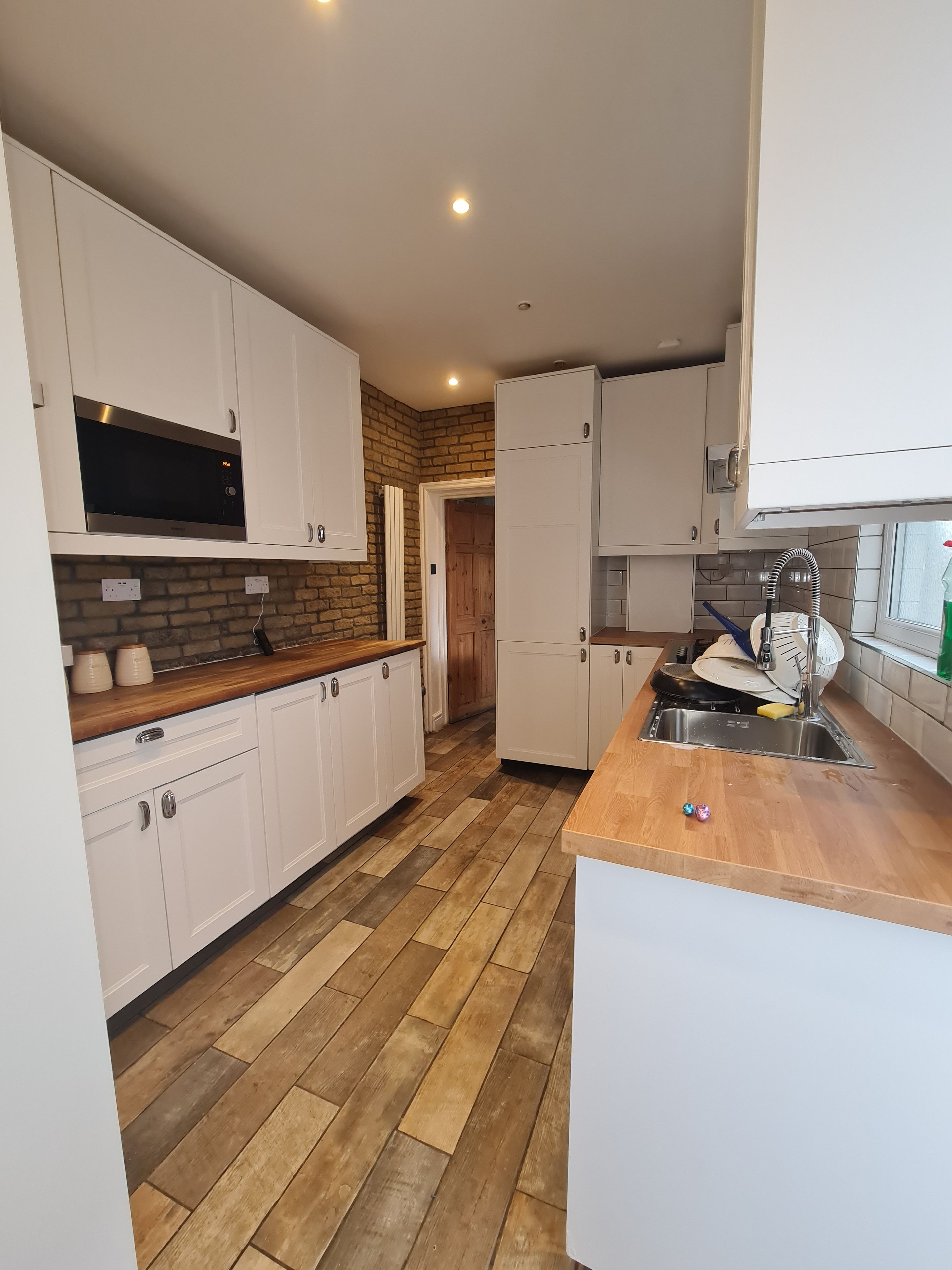 Una cocina moderna con armarios blancos, una encimera de madera y un microondas integrado.