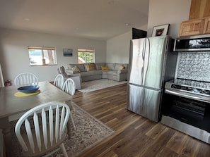 Cocina compacta equipada con refrigerador, microondas y horno. Zona de comedor con mesa y sillas.