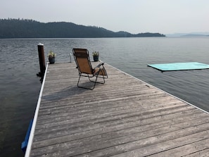 A wooden dock extending into calm water with a single folding chair and potted plants.