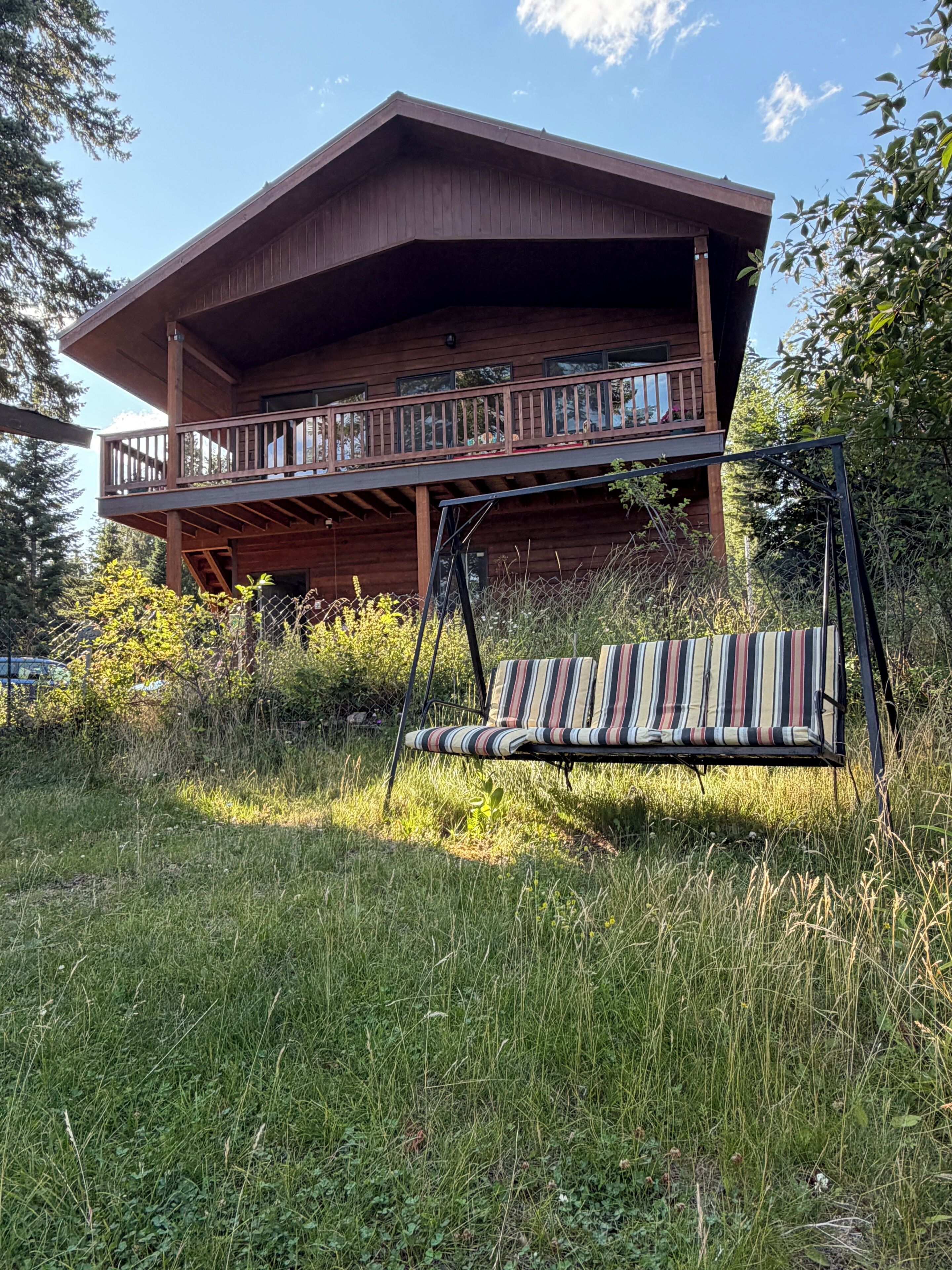 Une cabane en bois dotée d’un balcon, entourée d’herbes hautes et d’arbres.