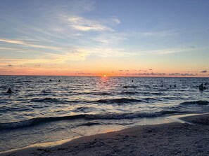Ein Strand bei Sonnenuntergang mit Wellen und Menschen im Wasser.