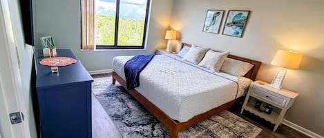 A bedroom with a bed, bedside tables, a desk, a ceiling fan, a window with curtains, and artwork on the wall.
