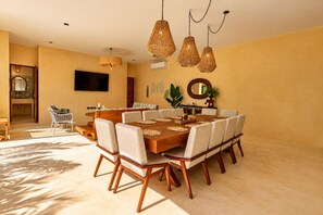 Un comedor con una mesa de madera, sillas blancas tapizadas y lámparas colgantes de mimbre.