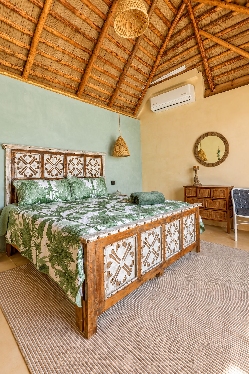 A room with a bed, a hanging light fixture, a mirror, and a wooden dresser.