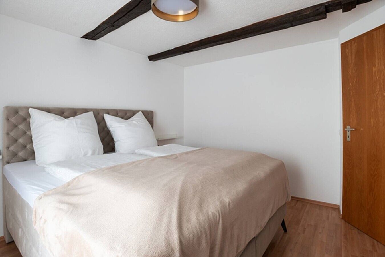 Ein Schlafzimmer mit einem Bett, weißer Bettwäsche, einer Holztür und freiliegenden Holzbalken an der Decke.