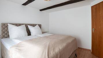 Ein Schlafzimmer mit einem Bett, weißer Bettwäsche, einer Holztür und freiliegenden Holzbalken an der Decke.