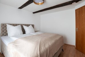 Une chambre à coucher avec un lit, du linge de lit blanc, une porte en bois et des poutres apparentes en bois au plafond.