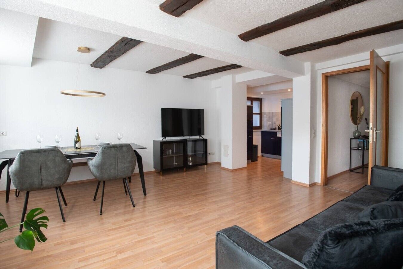 Una sala de estar moderna con televisor de pantalla plana, comedor con sillas y una mesa, y cocina al fondo.