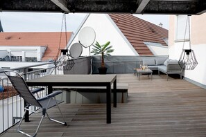 Une terrasse sur le toit, avec une table, des chaises, un canapé et un pot de fleurs.