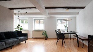 A modern living room with a black sofa, wooden flooring, and a dining area with a table and chairs.